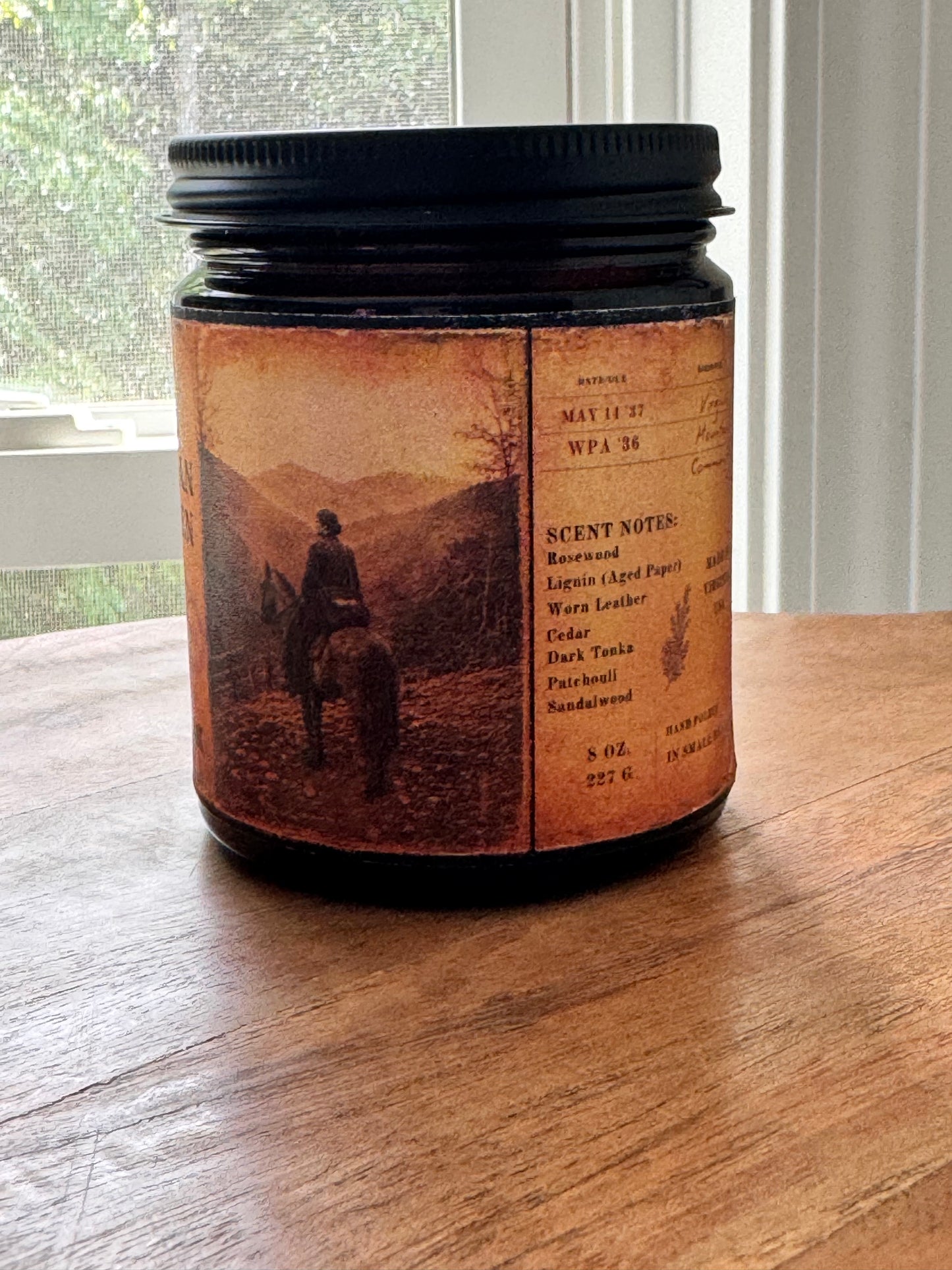 Vintage-inspired candle label featuring archival library card details, handwritten notes, and fragrance notes including rosewood, aged paper, cedar, leather, dark tonka, patchouli, and sandalwood. Printed on distressed parchment-style artwork wrapped around an amber candle vessel.