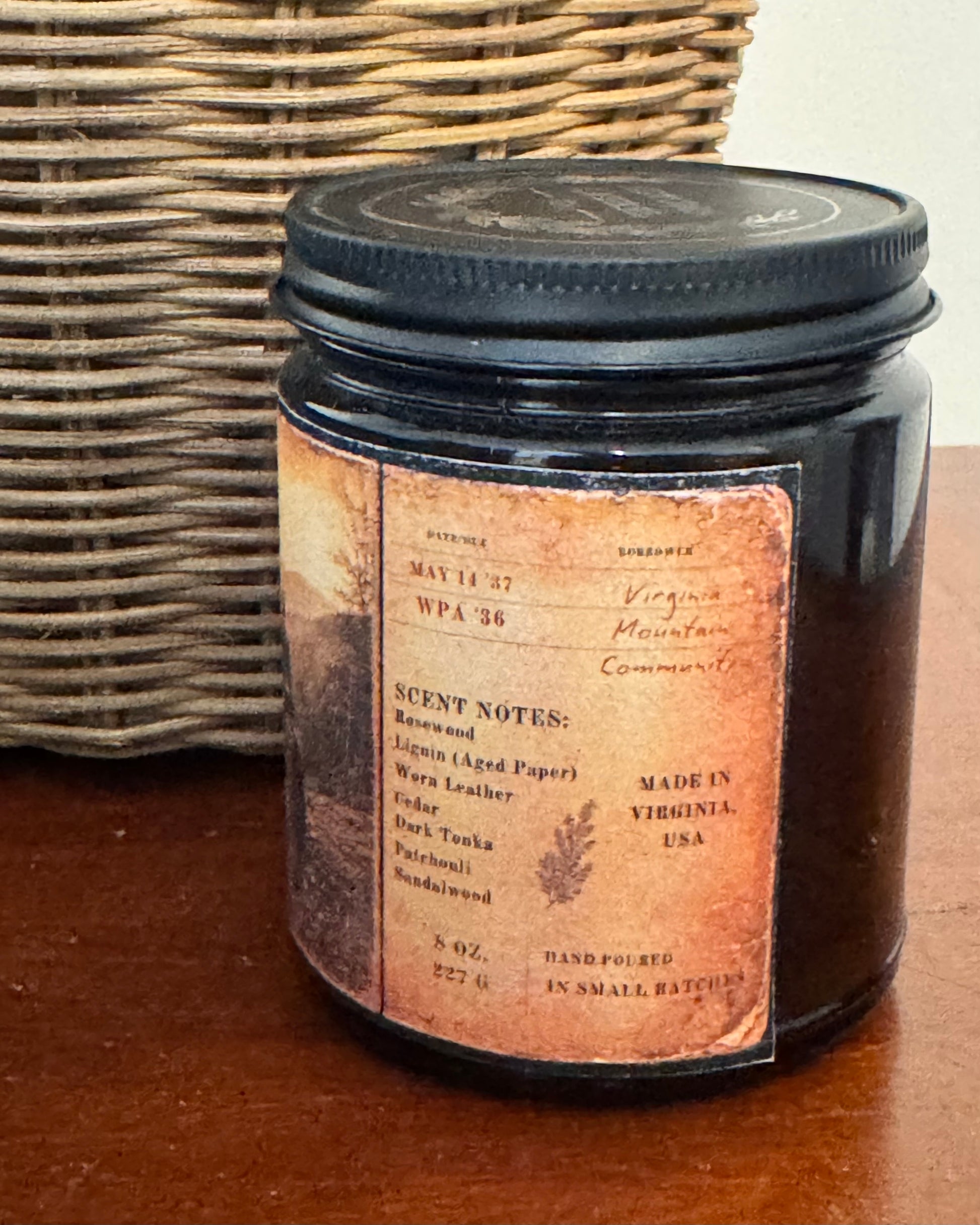 Vintage-inspired candle label featuring archival library card details, handwritten notes, and fragrance notes including rosewood, aged paper, cedar, leather, dark tonka, patchouli, and sandalwood. Printed on distressed parchment-style artwork wrapped around an amber candle vessel.