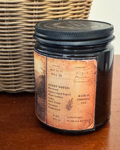 Vintage-inspired candle label featuring archival library card details, handwritten notes, and fragrance notes including rosewood, aged paper, cedar, leather, dark tonka, patchouli, and sandalwood. Printed on distressed parchment-style artwork wrapped around an amber candle vessel.