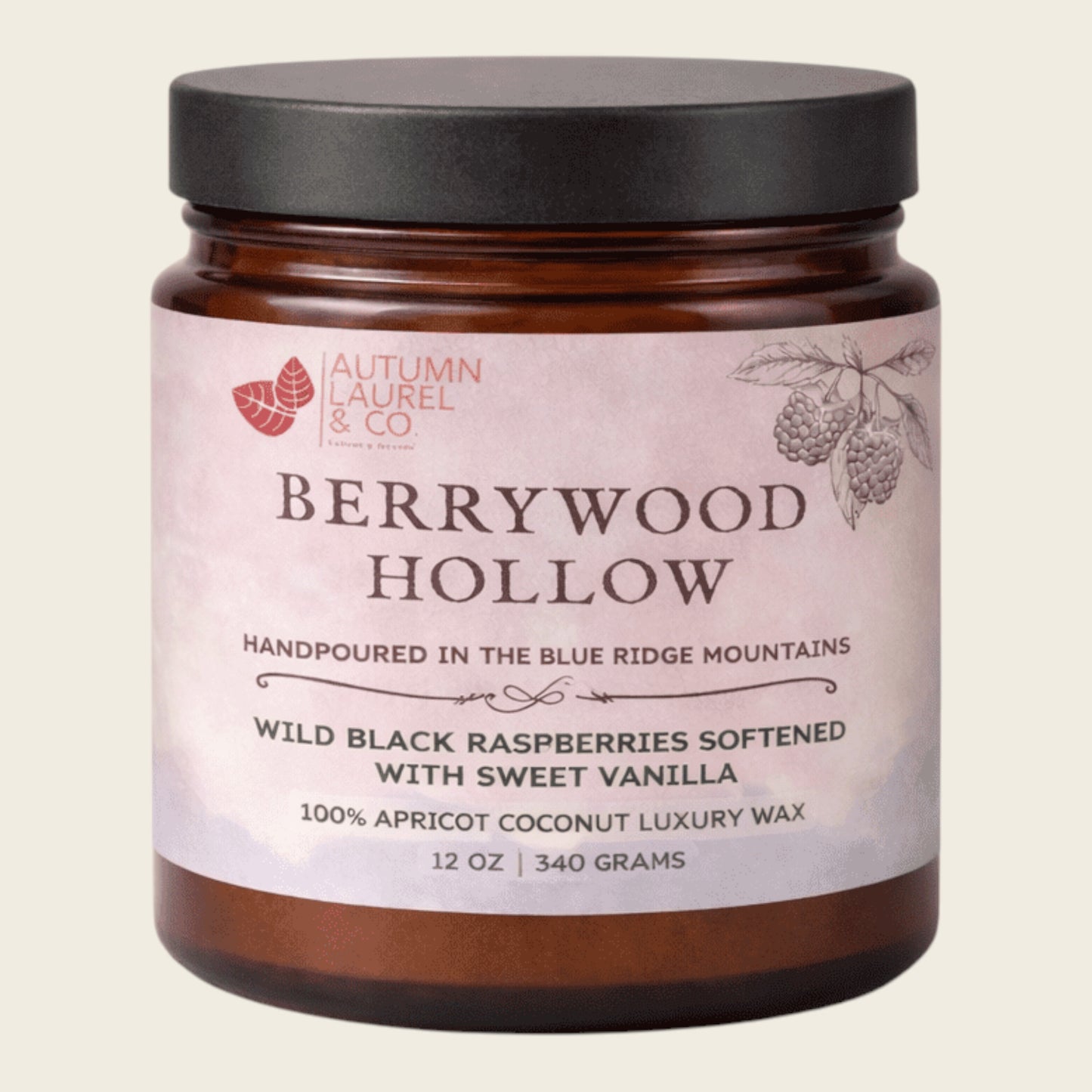 An amber glass jar candle with a black lid and a pale pink label reading 'Berrywood Hollow' by Autumn Laurel & Co, on a light beige background.