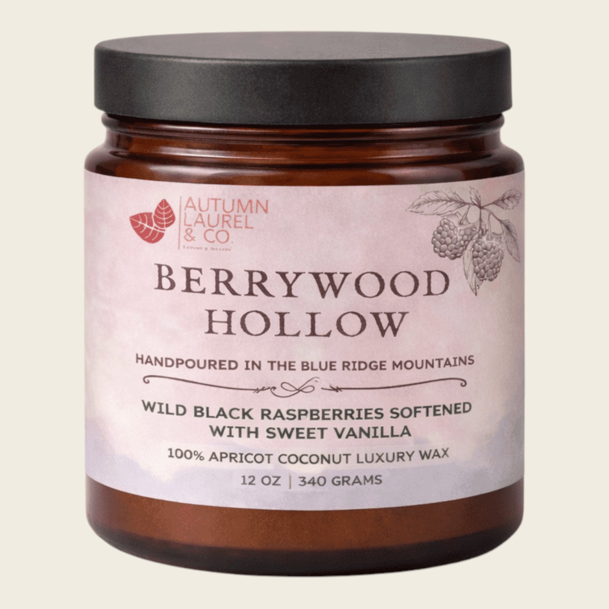 An amber glass jar candle with a black lid and a pale pink label reading 'Berrywood Hollow' by Autumn Laurel & Co, on a light beige background.