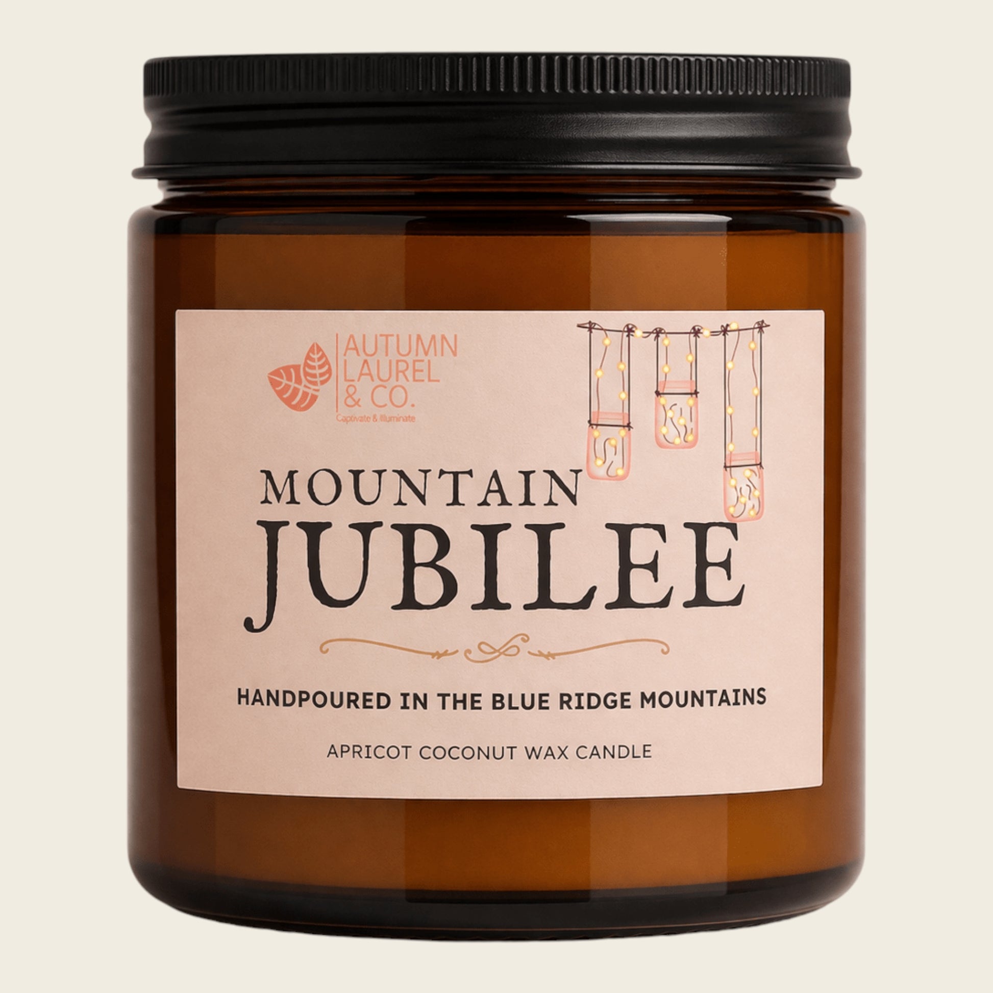 An amber glass jar candle with a black screw-top lid and a light pink label reading 'MOUNTAIN JUBILEE' by Autumn Laurel & Co., shown on a plain light beige background.