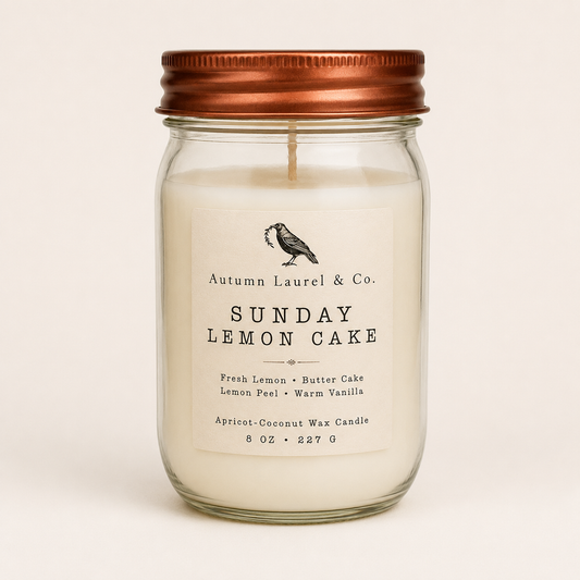A glass mason jar candle with white wax, a copper-colored metal lid, and a cream-colored paper label that reads 'Autumn Laurel & Co. SUNDAY LEMON CAKE'.